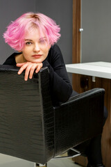 Portrait of a beautiful young caucasian woman with new short pink hairstyle sitting in a chair at a beauty salon