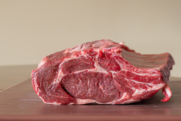 Wall Mural - A closeup of a large fresh prime rib beef roast that is sitting on a brown plastic cutting board in a restaurant. The juicy raw red meat has some white fat marbling and multiple rib bones.