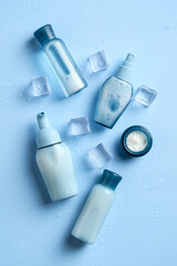 Wall Mural - Wet cosmetic bottles and jar with ice cubes on blue background. Set of skin moisturizing beauty products. Flat lay, top view.