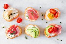Assortment Of Cream Cheese Crostini Hors D'oeuvres With A Variety Of Toppings. Above View On A White Marble Background. Party Food Concept.