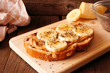 Wall Mural - Healthy breakfast toast with peanut butter, bananas and chia seeds on multi grain bread. Close up on a dark wood background.