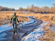 male cyclist is walking his bike through icy spots on a bike trail while commuting along Poudre River in Fort Collins, Colorado in winter scenery