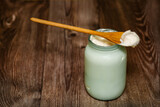 Fototapeta Sypialnia - homemade milk sour cream in a glass jar with a rustic wooden spoon. The village produces an agricultural product from milk. Delicious organic food.