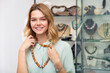 Portrait of cheerful girl trying on necklace made of natural stones in jewelry shop