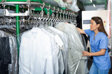 Positive Female Dry-cleaning Worker Preparing Garments For Collection, Hanging Clean Clothes Packed In Plastic Bags On Rail