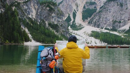 Wall Mural - young tourist hiker man reading map sitting by alpine lake lago di braies (pragser wildsee) in trent