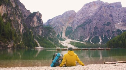 Wall Mural - young tourist hiker man listening to music sitting by alpine lake lago di braies (pragser wildsee) i