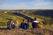 © Studio Romantic - Dreamy group of young hikers sitting on the edge of the mountain and looking into the distance.