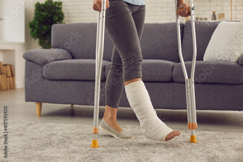 Young patient undergoes rehabilitation at home. Woman with broken leg in cast makes good progress and walks with crutches in the living-room. Domestic life and successful recovery after car accident
