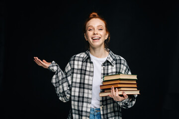 laughing young woman college student holding books and looking at camera on isolated black backgroun