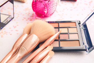 Set of makeup brushes with cosmetics on light background