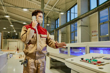 Wall Mural - Factory worker talking on the phone while supervising automated woodworking machine during coronavirus pandemic.