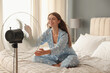© New Africa - Woman enjoying air flow from fan on bed in room. Summer heat