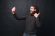 © Vulp - Cheerful bearded man over black background taking selfie with smartphone.