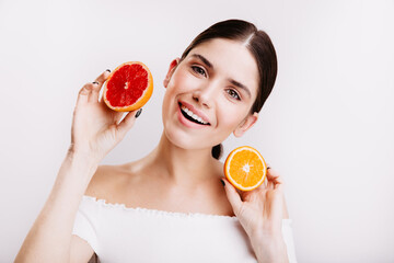 Sticker - Adorable girl with friendly smile looks into camera on white background. Woman without makeup holds slices of juicy orange and grapefruit