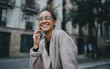 © Roman - Portrait of young good-looking Caucasian woman wearing glasses, talking on her smartphone outdoors and smiling sweetly. Mobile digital devices make communication and interaction between people easier