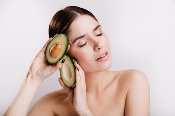 Sticker - Snapshot of girl without makeup on white background. Lady with closed eyes keeps healthy avocado