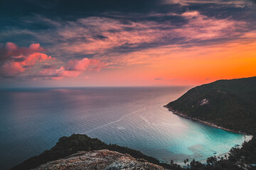 Asia sunset aerial: ocean island highland at Tanote Bay, Koh Tao, Thailand. Amazing Thai skyscape in warm sun set tones on water reflection. Green trees on hills, sand beach at asian lagoon