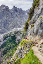 Vertical Shot Of A Person Standing On A Narrow Hiking Path On Rocky Hills Under The Sunlight