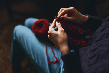 Female hands knitting with red yarn.