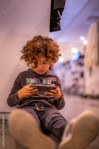 Young boy (4-5) playing mobile game on his parents\' phone in a shopping arcade