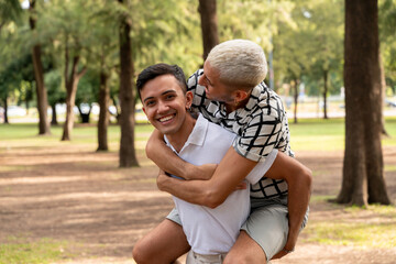 Wall Mural - Young gay guy giving a piggyback ride in a public park