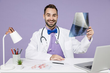 Wall Mural - Smiling cheerful young bearded doctor man wearing medical suit gown stethoscope hold X-ray of lungs fluorography roentgen isolated on violet background. Healthcare personnel health medicine concept.