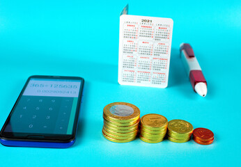 Sticker - Smartphone, ballpen, 2021 calendar, and coins stacked on top of each on blue background