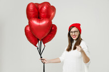 Smiling Young Woman In Basic Sweater Red Hat Glasses Pointing Index Finger Camera On You Celebrating Birthday Holiday Party Hold Bunch Heart Air Inflated Helium Balloons Isolated On White Background.