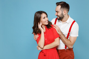 Wall Mural - Smiling cheerful young couple two friends man woman in white red clothes hugging looking at each other isolated on pastel blue color background studio portrait. St. Valentine's Day holiday concept.