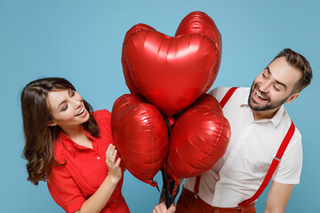 Sticker - Excited young couple friends man woman in white red clothes celebrating birthday holiday party hold bunch air inflated helium balloons looking at each other isolated on blue color background studio.