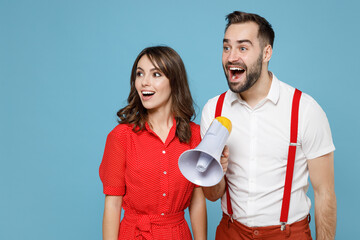 Poster - Surprised young couple two friends man woman wearing white red clothes scream in megaphone looking aside isolated on pastel blue color background studio portrait. St. Valentine's Day holiday concept.