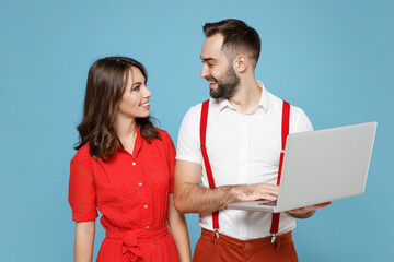 Wall Mural - Smiling young couple two friends man woman in white red clothes working on laptop pc computer looking at each other isolated on blue color background in studio. St. Valentine's Day holiday concept.