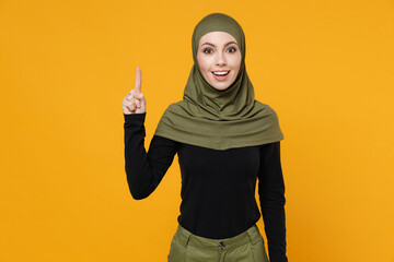 Wall Mural - Excited young arabian muslim woman in hijab black green clothes holding index finger up with great new idea isolated on yellow color background studio portrait. People religious lifestyle concept.