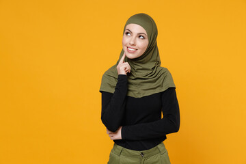 Wall Mural - Pensive young arabian muslim woman wearing hijab black green clothes put hand prop up on chin looking aside up isolated on yellow color background, studio portrait. People religious lifestyle concept.