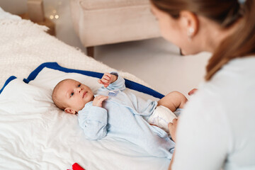 loving, caring mother changes clothes for a baby lying on his back on the bed