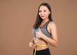 © mikhail_b_azarov - A slender woman measures her waist with a measuring tape. n a brown background.