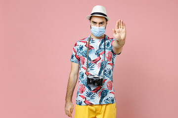 Wall Mural - Young traveler tourist man in face mask to safe from coronavirus virus covid-19 showing stop gesture with palm isolated on pink background. Passenger travel on weekend. Air flight journey concept.