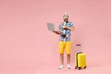 Wall Mural - Full length of excited young traveler tourist man pointing index finger on laptop pc computer booking hotel isolated on pink background. Passenger traveling on weekends. Air flight journey concept.