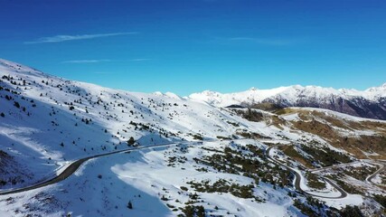 Wall Mural - An aerial view of a car driving on spiral road with trees on a snowy mountainside in 4K