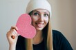 Beauty portrait of smiling blonde young woman with pretty pink heart. Big paper heart in the hands.Cupid day.
