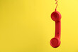 Red corded telephone handset hanging on yellow background, space for text. Hotline concept