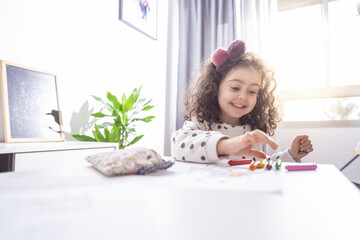 Wall Mural - Shallow focus shot of a happy little girl painting with colorful crayons