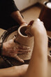 the hands of a girl and a man stained with clay make a jug on a potter's wheel