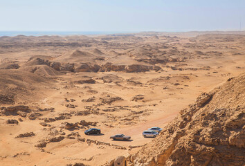 Four cars are parked in the desert. The sea on the horizon