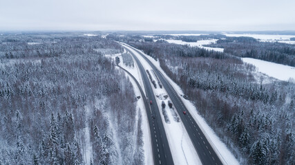 Wall Mural - Beautiful road through the forest. Winter natural landscape. Cloudy snowy day.  Bird's eye. Travel concept