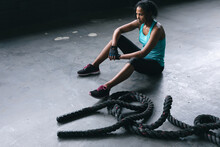 African American Woman Wearing Sports Clothes Sitting Resting After Battling Ropes In Empty Urban Bu