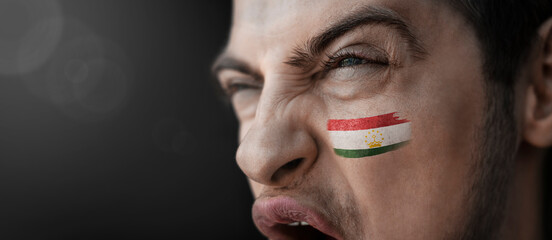 A screaming man with the image of the Tajikistan national flag on his face