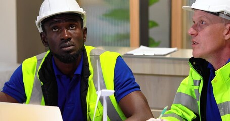 Wall Mural - Two engineers African american engineer and caucasian electrician wearing white hard hat working on laptop computer at workplace office. clean and green alternative energy concept.