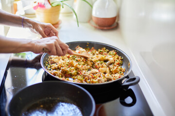 Woman hands moving rice with chicken and vegetables in paella pan